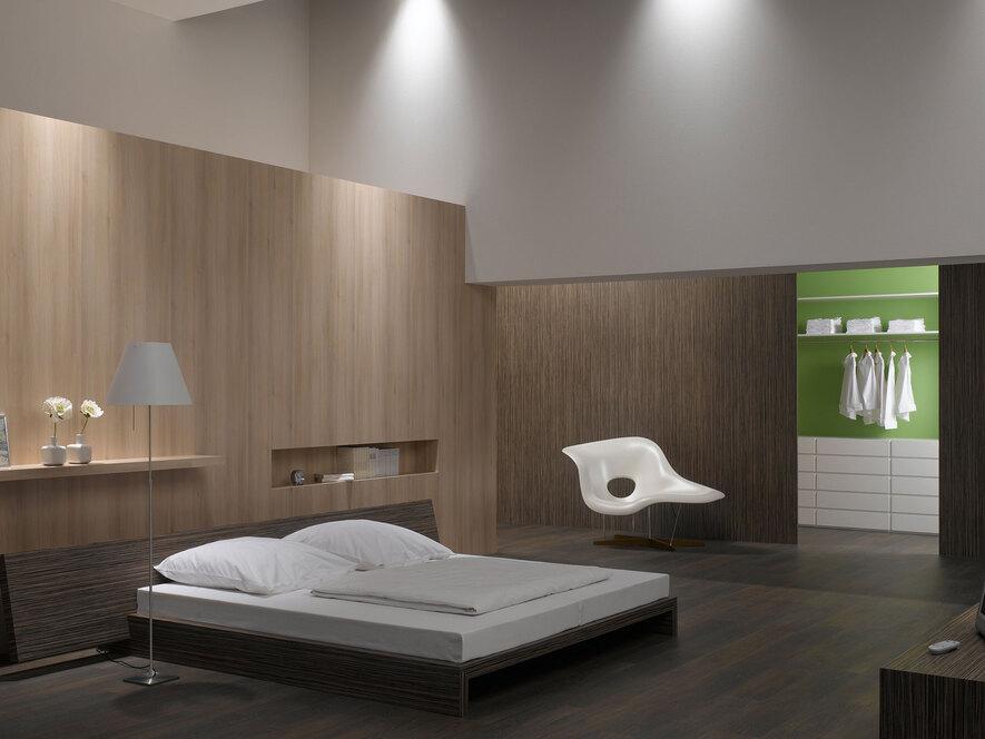 Schlafzimmerimpression mit Holzverkleidung an Wand Schlafzimmerimpression von Bett, Nachtisch und Sideboard mit Holzverkleidung an Wand und indirektert Beleuchtung